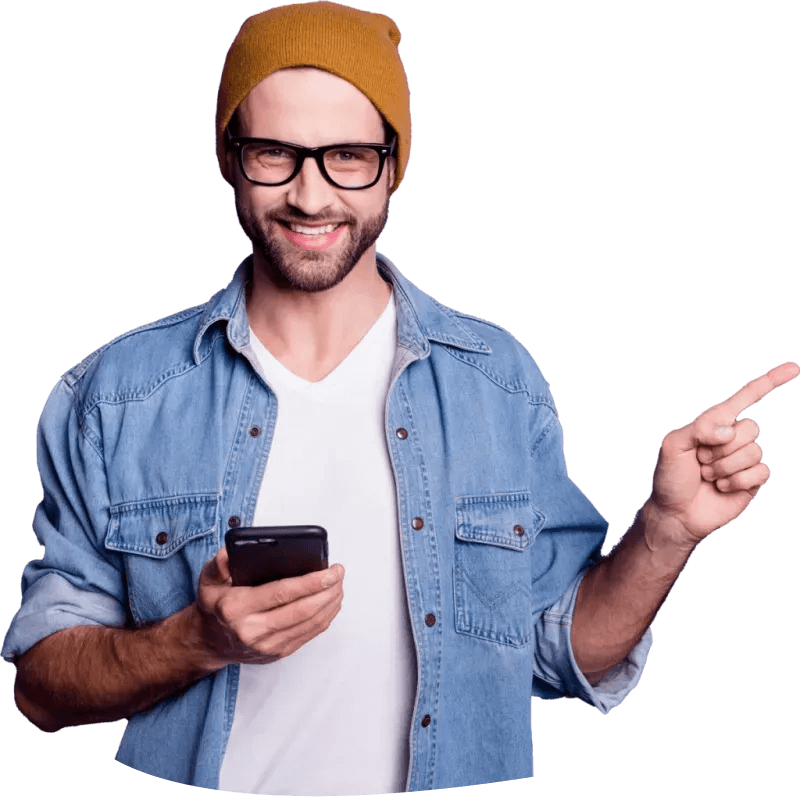 Zu sehen ist ein junger Mann, mit Jeanshemd und einer braunen Mütze. Er hat sein Handy in der linken Hand und zeigt mit der rechten Hand auf etwas